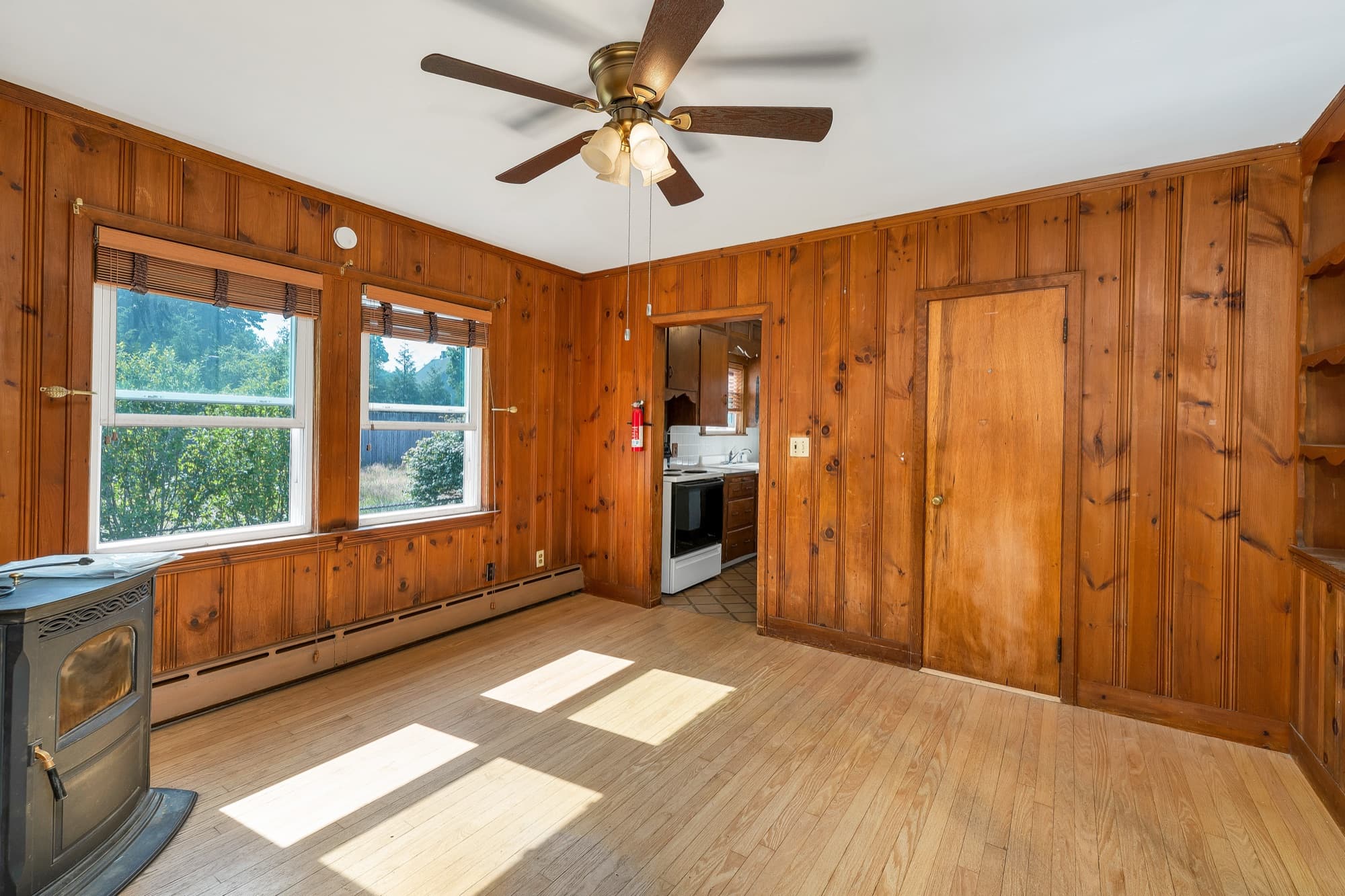 Wood-paneled living room with a ceiling fan and a wood stove