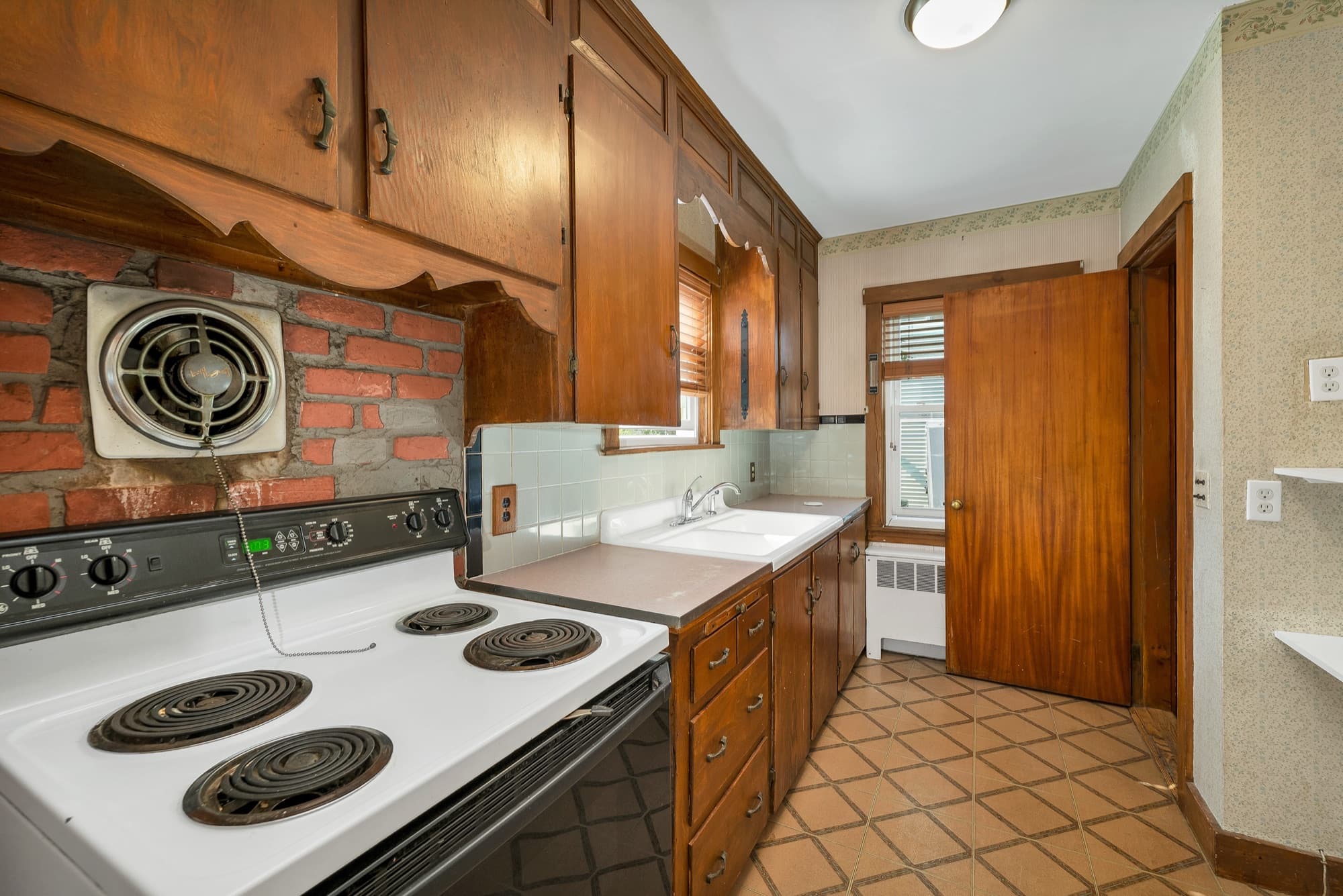 Kitchen with wood cabinetry, an electric range, and a brick backsplash